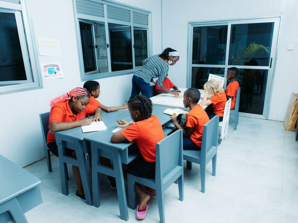 Teacher instructing children at tables in a classroom, representing the individual identity of a school