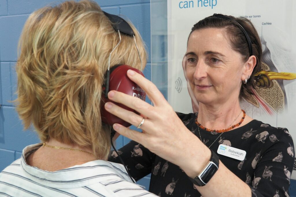 An audiologist helping a woman with a hearing test, headphones being placed on her before testing