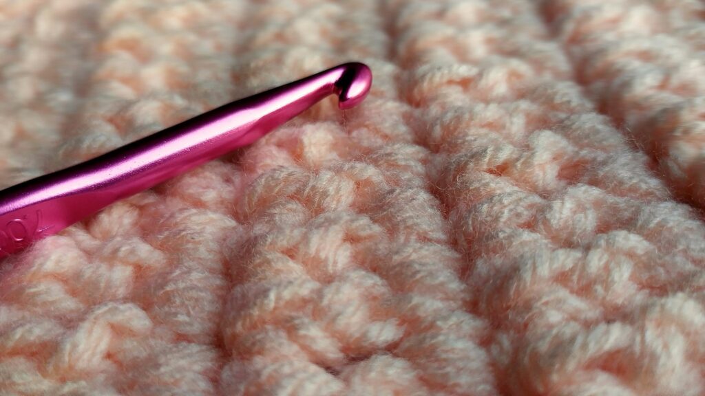 A pink and silver crochet hook on white fabric, one of the basic tools for crocheting