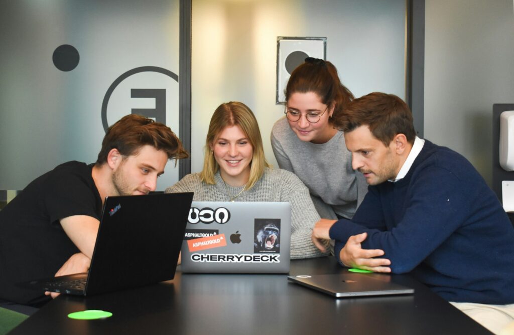 Four people collaborating around a laptop in a modern office, as a tech PR team might