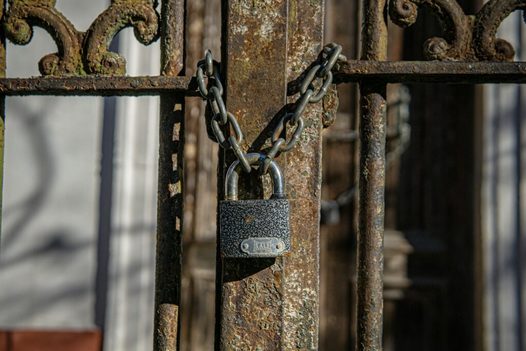 A rusty metal gate secured with a padlock and chain, showing the effects of corrosion